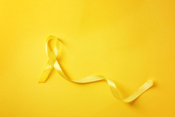 Yellow ribbon on color background. Cancer concept - Φωτογραφία, εικόνα