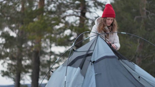 Attrayant jeune femme touristique dans un chapeau rouge recueille une tente touristique près de la forêt sur la côte 4k
 - Photo, image