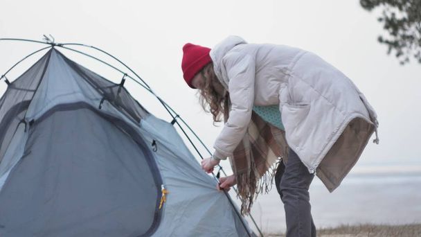 赤い帽子の魅力的な若い観光客女性が海岸の森の近くの観光テントを収集します。 - 写真・画像