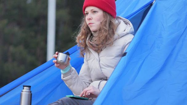 Vonzó fiatal nő turisztikai a red hat turisztikai sátorban ül, és italok tea egy Termosz - Fotó, kép