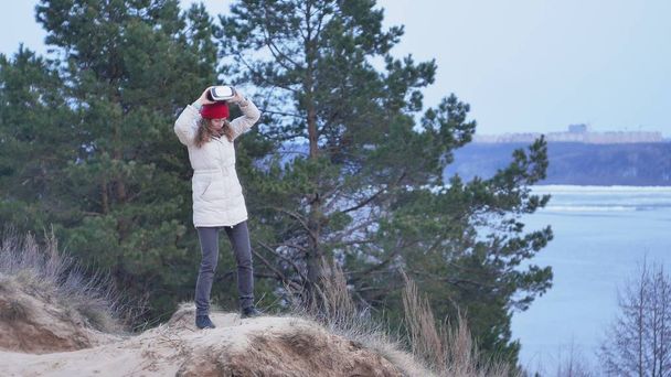 A red hat vonzó fiatal nő turisztikai ül egy partján, és élvezi a virtuális-valóság sisak - Fotó, kép