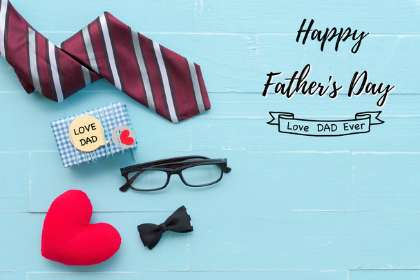 Ευτυχισμένος πατέρες ημέρα έννοια. Κόκκινη γραβάτα, γυαλιά, δώρο κουτί με αγάπη ο μπαμπάς κείμενο και χειροποίητο κόκκινο καρδιά σε φόντο φωτεινό μπλε παστέλ ξύλινο τραπέζι. - Φωτογραφία, εικόνα