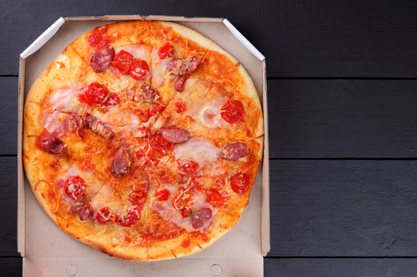 Pizza sobre fondo de madera negra, pizza italiana con tomates, tocino, salchichas y queso, comida rápida, comida festiva sobre fondo oscuro, espacio para copiar
 - Foto, imagen