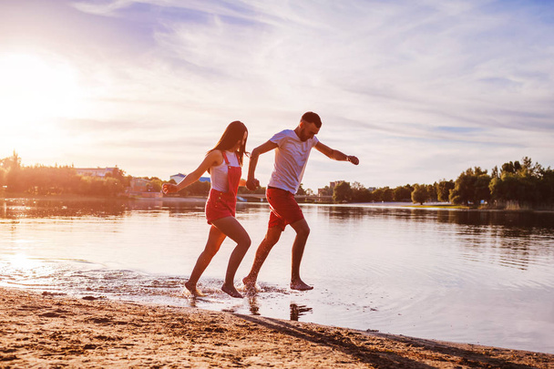 Nuori mies ja nainen juoksemassa joen rannalla. Rakastavaiset pitävät hauskaa auringonlaskun aikaan. Kaverit jäähdytys ja nauttia vapaudesta
 - Valokuva, kuva