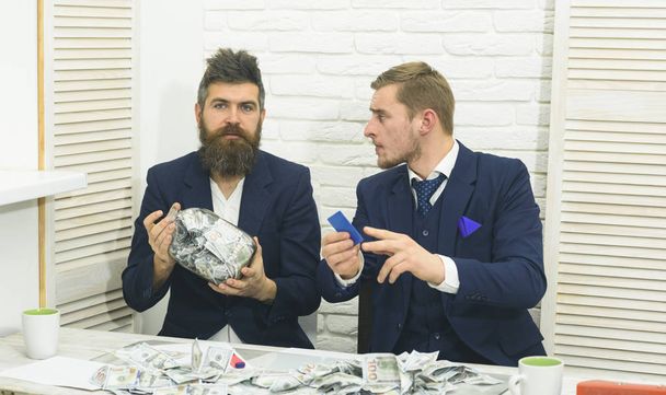 Cash issues concept. Colleagues collecting money in jar instead of bank account. Business partners, businessmen at meeting in office. Manager with beard and colleague with jar of cash and card - Photo, image