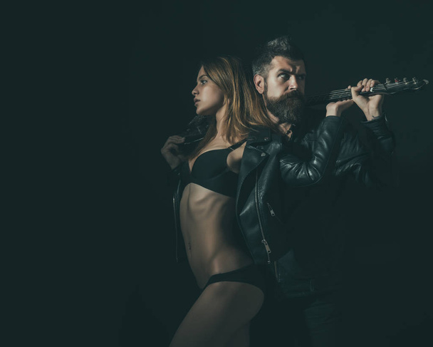 Couple in love cuddling with guitar, black background. Couple sexy and brutal posing with guitar. Rock and roll concept. Guitarist with beard and sexy girl in bra enjoy rock and roll lifestyle - Foto, immagini