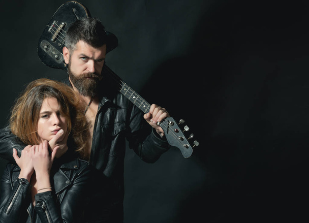 Couple in love cuddling with guitar, black background. Rock and roll concept. Guitarist with beard and sexy girl in bra enjoy rock and roll lifestyle. Couple sexy and brutal posing with guitar - Φωτογραφία, εικόνα