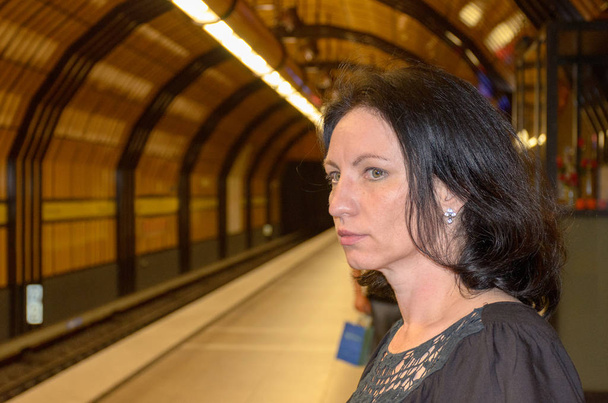 Nuori nainen tuijottaa innokkaasti metroaseman raiteita odottaessaan junan saapumista.
 - Valokuva, kuva