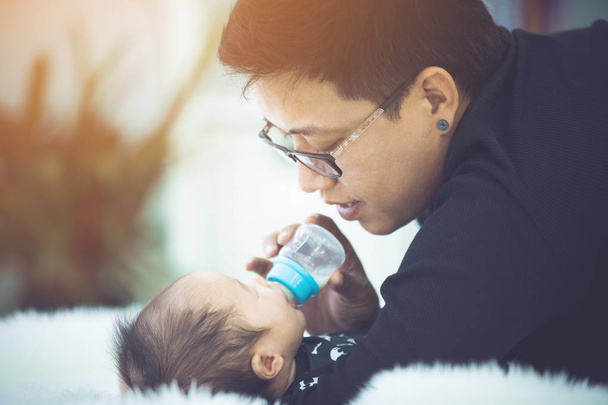Szczęśliwy ojciec Azjatycka karmienia mleko z butelki mleka na córeczkę z twarzy uśmiech. - Zdjęcie, obraz
