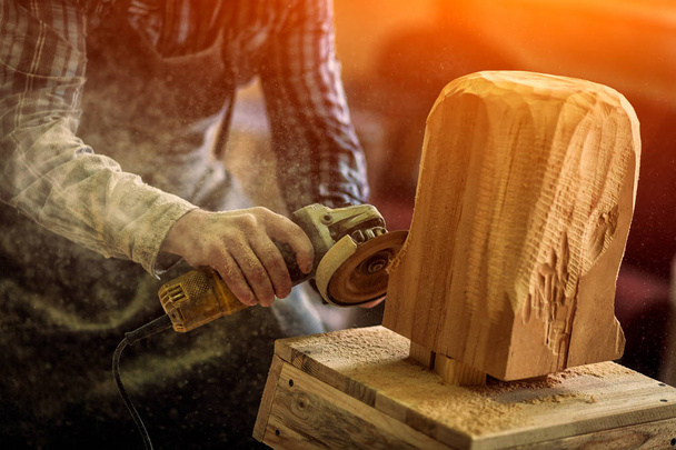 Primer plano de un carpintero en ropa de trabajo y pequeño propietario de la compra que trabaja en el taller de carpintería, procesa la placa con una amoladora angular, sobre la mesa es un martillo y muchas herramientas
  - Foto, Imagen