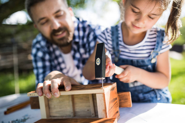 Father with a small daughter outside, making wooden birdhouse. - Fotoğraf, Görsel