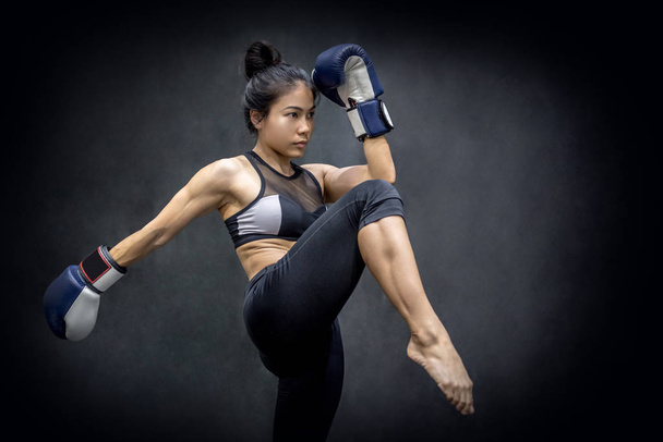 Genç Asyalı kadın boksör mavi boks eldivenleri dövüş sanatları siyah arka plan üzerinde egzersiz spor salonunda, tekme ile - Fotoğraf, Görsel