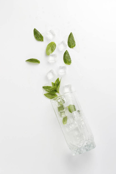 Spilled Glass with refreshing water, mint leaves and ice cubes on a light background. - Foto, afbeelding