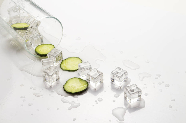 Gemorste glas met verfrissende water, plakjes komkommer en ijsblokjes tegen een lichte achtergrond. - Foto, afbeelding