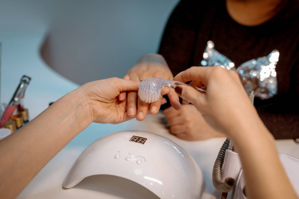 Beautician polishing female nails with nail file in beauty salon - 写真・画像
