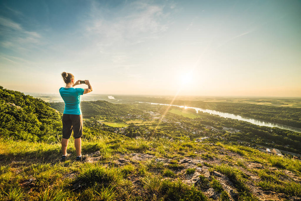 A Girl Standing on the Edge of the Cliff and Taking Photograph of the Sunset and the Valley with the River - Photo, Image