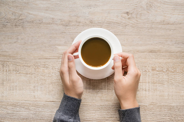 weibliche Hand hält eine Tasse Kaffee auf Holz Textur Hintergrund. - Foto, Bild