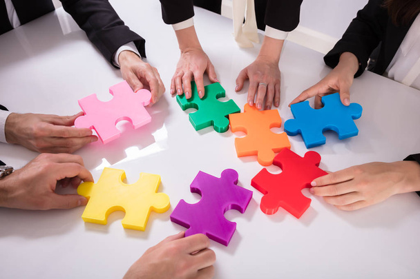 Grupo de Empresarios Resolviendo rompecabezas multicolor en el escritorio
 - Foto, Imagen