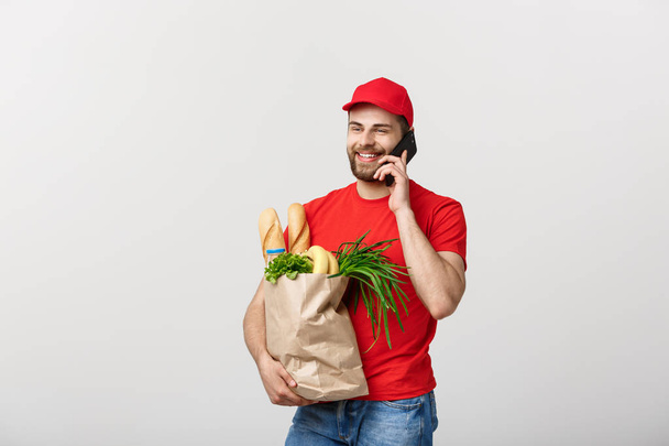 Handsome grocery delivery man talking to mobile and holding grocery paper bag. - Photo, Image