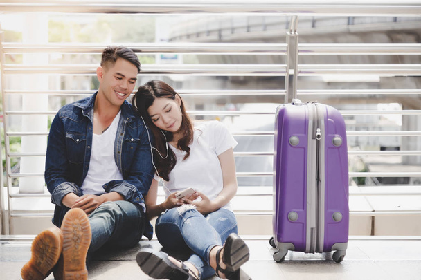 Handsome boyfriend and beautiful girlfriend take a rest and listening music together. Traveler couple get honeymoon at foreign country. They look romantic and sweet. They wear jeans. city background - Photo, image