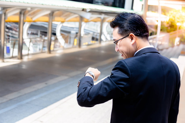 A handsome businessman is looking wristwatch for checking time. Handsome guy feels happy when he comes to meeting point and has ample time. He feel relieved. He wears full suit. space, city background - Photo, Image