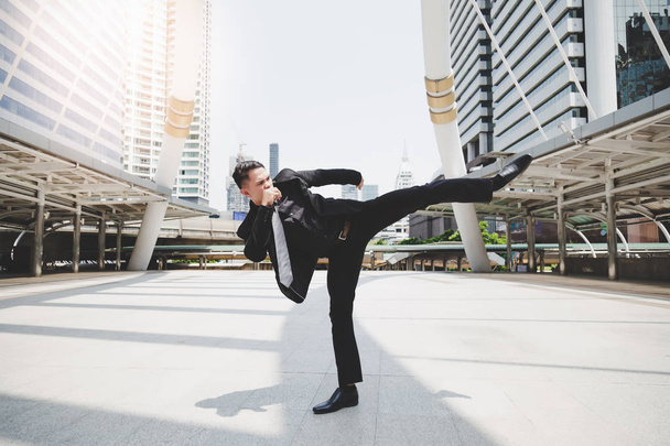 Handsome businessman get angry his boss and wants to relieve stress and furious. Cool guy is exercising by kicking on the air. Attractive man wears suit, necktie, long trousers. cityscape background - Photo, image