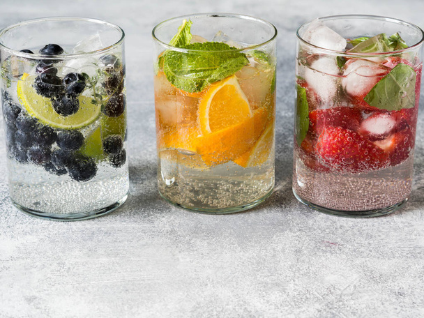 Set of summer healthy cocktails, various citrus infused waters, lemonades or mojitos, with lime and blueberries, orange and strawberries and basil, diet detox beverages, in different glasses - Photo, Image