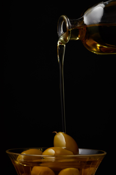 huile d'olive verser dans un bol avec des olives de bouteille isolée sur noir
 - Photo, image