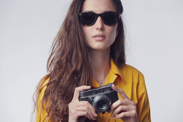 Portrait of Young beautiful woman wearing sunglasses and holding photography vintage camera - Фото, изображение