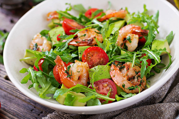Fresh salad bowl with shrimp, tomato, avocado and arugula on wooden background close up. Healthy food. Clean eating. - Photo, Image