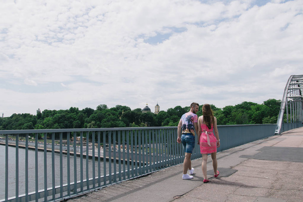 Pareja joven abrazándose y sonriéndose caminando en un puente
 - Foto, Imagen