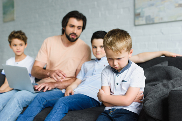 selective focus of upset little boy and family man with laptop near by on sofa at home - Foto, immagini