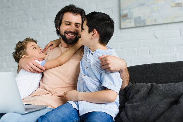 portrait of man with laptop and kids near by hugging each other on sofa at home - Fotoğraf, Görsel