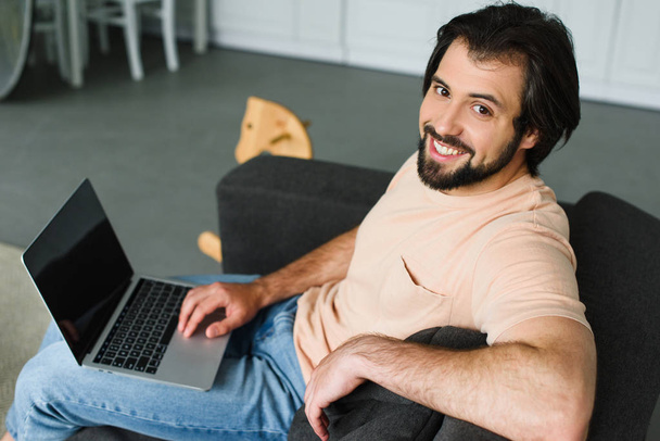 side view of smiling man with laptop resting on sofa at home - 写真・画像