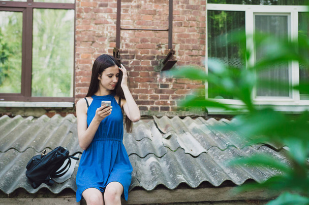 Une fille très belle et joyeuse se tient dans la rue avec de longs cheveux luxueux et s'assoit avec son téléphone
 - Photo, image
