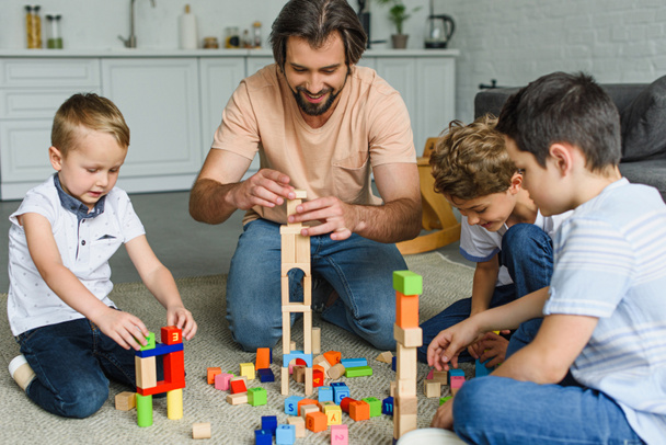 alegre padre e hijos jugando con bloques de madera juntos en el suelo en casa
 - Foto, Imagen