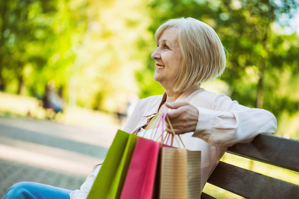 glückliche erwachsene Frau sitzt nach dem Einkaufen im Park.  - Foto, Bild