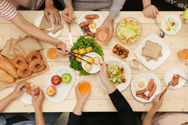 Disfrutando de la cena con amigos. Vista superior del grupo de personas cenando juntas sentadas en la mesa de madera
 - Foto, imagen
