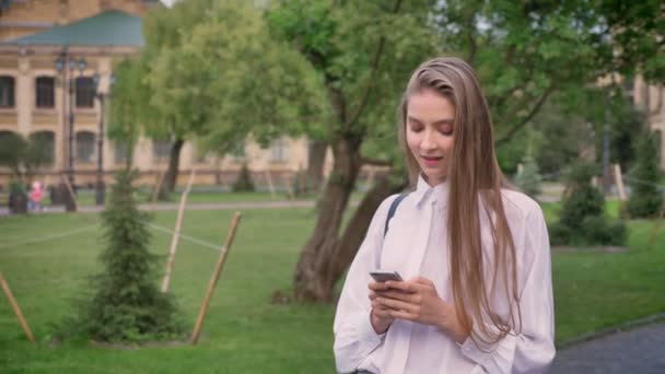 Young beautiful girl types messages on her smartphone in summer, flirt conception, communication concept - Felvétel, videó