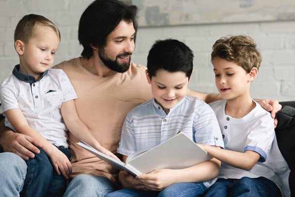 portrait of father and sons reading book together at home - Photo, Image