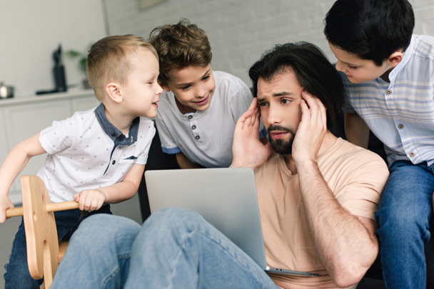portrait de père stressé avec ordinateur portable et petits enfants autour à la maison
 - Photo, image