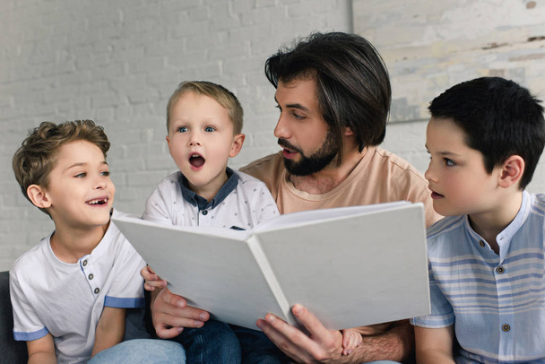 portrait of father and little sons reading book together at home - Fotoğraf, Görsel