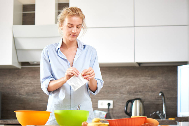 attractive blonde woman opening pack with spice while cooking dessert at kitchen - Foto, Bild