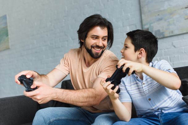 portrait of smiling father and son playing video games together at home - Zdjęcie, obraz