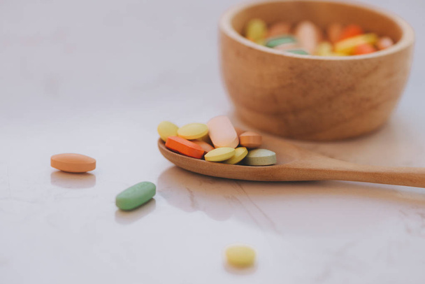 Assorted pharmaceutical medicine pills, tablets and capsules in wooden bowl and spoon - Photo, Image
