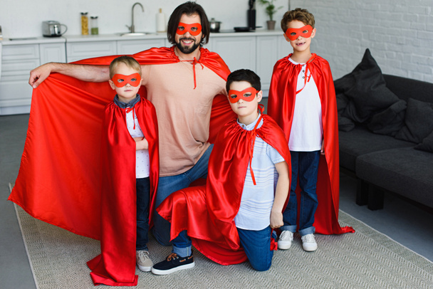 padre sorridente e figli piccoli in costume da supereroe rosso a casa
 - Foto, immagini