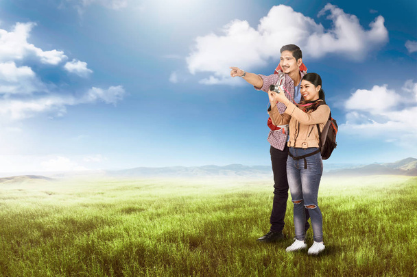 Happy asian couple tourist look around and taking photos on meadow field - Zdjęcie, obraz