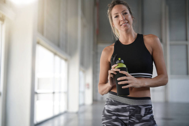Athletic woman standing in fitness room with water bottle - Foto, Imagem