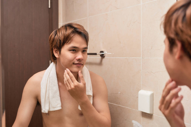 Belleza masculina. joven guapo asiático hombre tocando su suave cara después de afeitarse
 - Foto, Imagen
