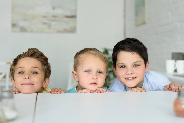 little boys hiding behind table and looking at camera at home - Foto, immagini